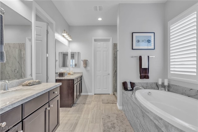 full bathroom with a marble finish shower, two vanities, a sink, a garden tub, and a wealth of natural light