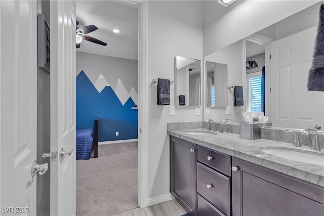 ensuite bathroom with double vanity, baseboards, a ceiling fan, and a sink