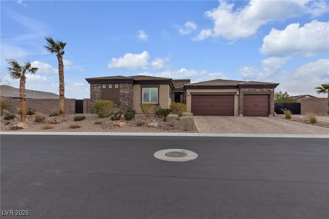 view of front of property with stucco siding, decorative driveway, stone siding, fence, and a garage