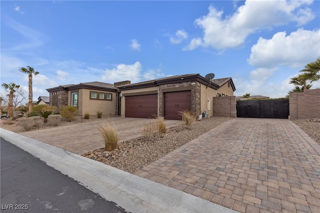 view of front facade with stucco siding, an attached garage, decorative driveway, and a gate