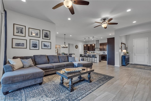 living room featuring recessed lighting, ceiling fan with notable chandelier, light wood-type flooring, and baseboards