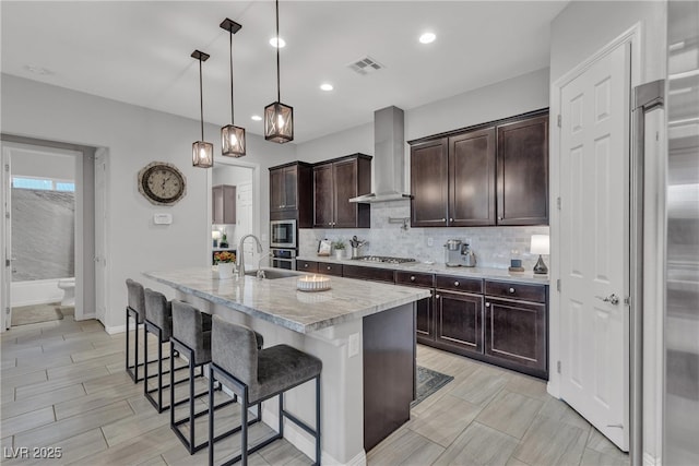 kitchen with visible vents, a breakfast bar, tasteful backsplash, dark brown cabinetry, and wall chimney range hood