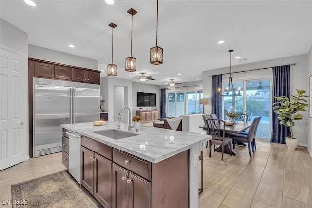 kitchen with a sink, light stone counters, appliances with stainless steel finishes, ceiling fan, and hanging light fixtures