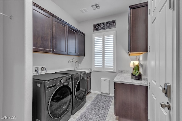 laundry area with visible vents, light wood-style flooring, separate washer and dryer, cabinet space, and a sink