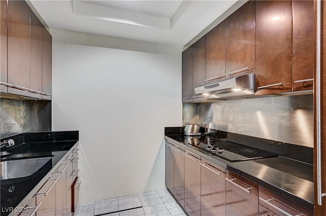 kitchen with under cabinet range hood, backsplash, dark countertops, and a sink