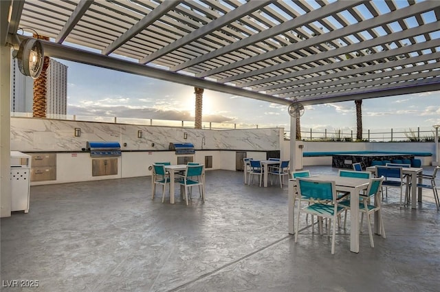 patio terrace at dusk featuring outdoor dining area, grilling area, exterior kitchen, and fence