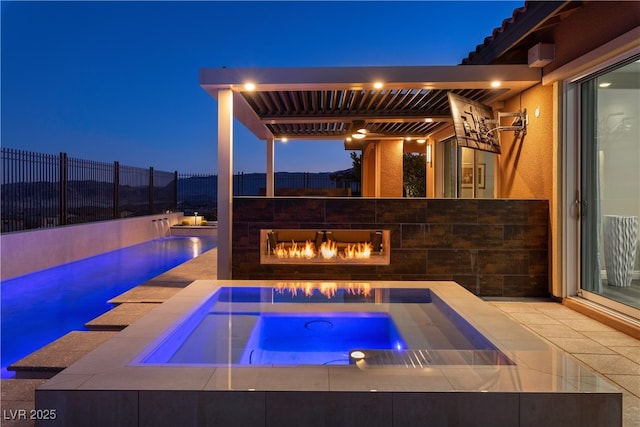 pool at twilight with a glass covered fireplace, an in ground hot tub, and a fenced backyard