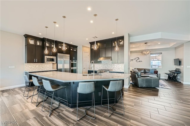 kitchen featuring a sink, built in appliances, a spacious island, and light countertops