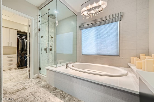 bathroom with a spacious closet, an inviting chandelier, a stall shower, and a garden tub