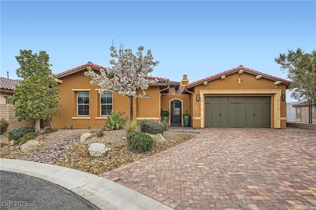 mediterranean / spanish-style home with fence, stucco siding, a garage, a tile roof, and decorative driveway