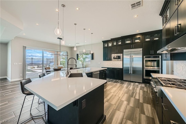 kitchen with built in appliances, dark cabinets, visible vents, and a sink