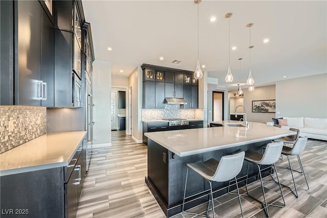 kitchen with under cabinet range hood, a kitchen breakfast bar, light countertops, and a sink