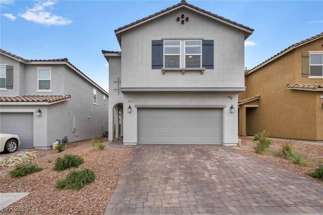 traditional-style house with a tile roof, decorative driveway, a garage, and stucco siding