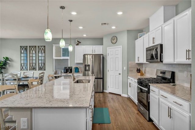 kitchen featuring a kitchen island with sink, a sink, backsplash, appliances with stainless steel finishes, and white cabinets