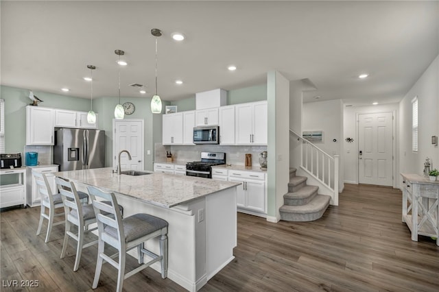 kitchen with a center island with sink, a sink, dark wood-style floors, appliances with stainless steel finishes, and white cabinets