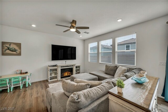 living area featuring a glass covered fireplace, visible vents, wood finished floors, and ceiling fan