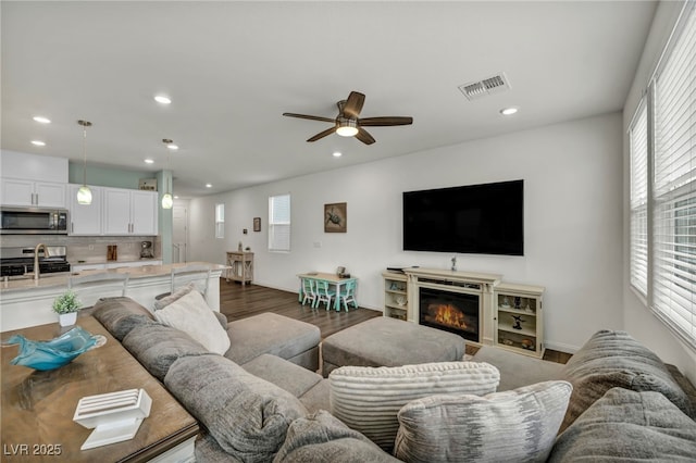 living room featuring visible vents, a healthy amount of sunlight, ceiling fan, and dark wood-style flooring