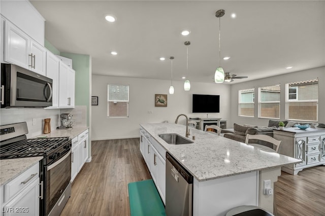 kitchen with wood finished floors, a center island with sink, stainless steel appliances, and a sink