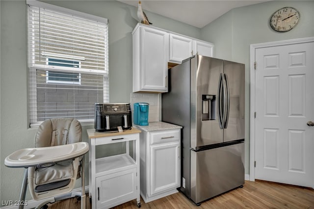kitchen featuring light stone countertops, light wood-type flooring, decorative backsplash, stainless steel refrigerator with ice dispenser, and white cabinets