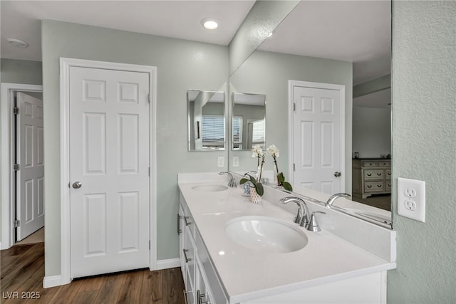 full bath with double vanity, wood finished floors, baseboards, and a sink