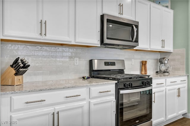 kitchen with light stone counters, backsplash, appliances with stainless steel finishes, and white cabinetry