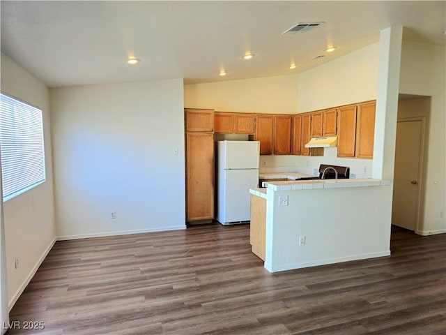 kitchen featuring tile countertops, visible vents, dark wood-style flooring, freestanding refrigerator, and under cabinet range hood