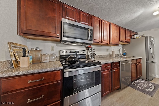 kitchen featuring light stone counters, stainless steel appliances, light wood-style floors, a textured ceiling, and a sink