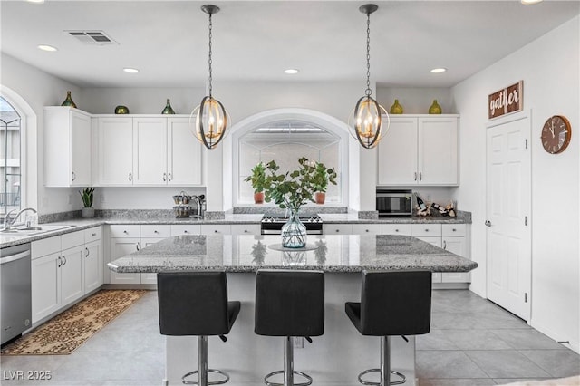 kitchen featuring a breakfast bar area, a sink, stainless steel appliances, white cabinets, and a center island