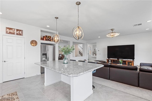 kitchen with light stone counters, visible vents, a kitchen island, stainless steel refrigerator with ice dispenser, and a chandelier