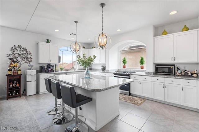 kitchen with a kitchen island, light stone countertops, a breakfast bar, white cabinets, and stainless steel appliances