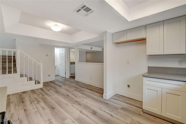 kitchen featuring visible vents, a raised ceiling, baseboards, and light wood-style flooring