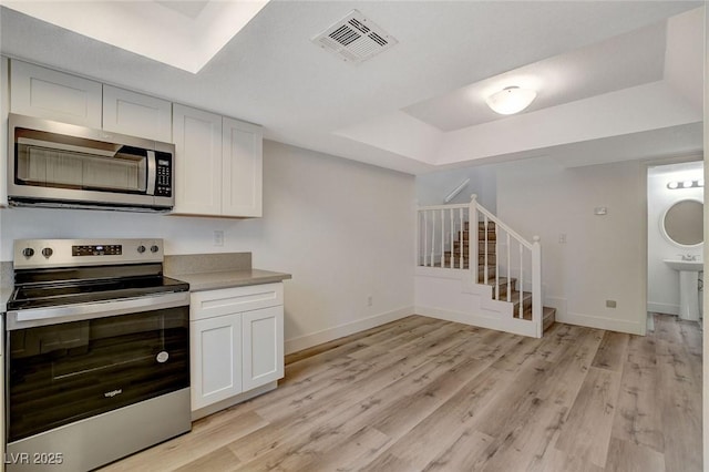 kitchen featuring visible vents, light wood-style flooring, stainless steel appliances, and a tray ceiling