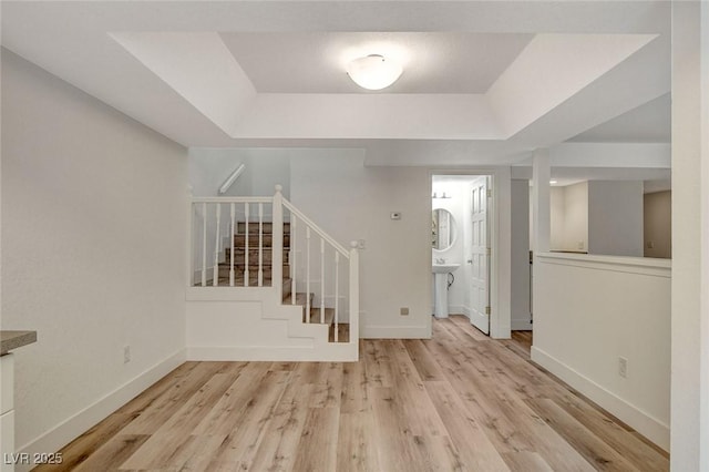 foyer with stairs, a raised ceiling, wood finished floors, and baseboards