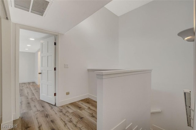 hall with wood finished floors, visible vents, and baseboards