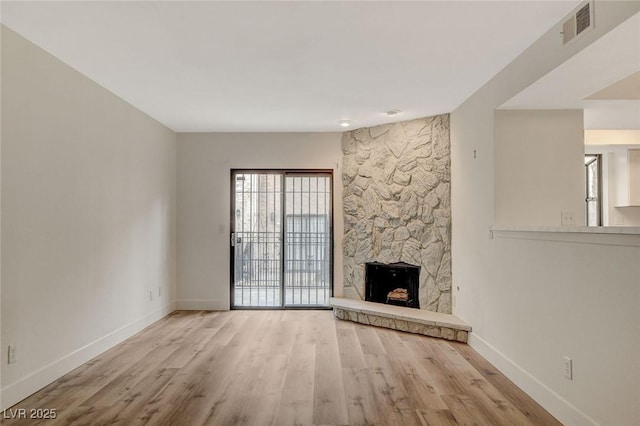 unfurnished living room with a stone fireplace, wood finished floors, visible vents, and baseboards