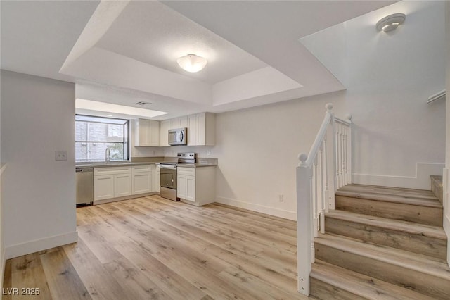 kitchen with light wood finished floors, baseboards, appliances with stainless steel finishes, white cabinetry, and a raised ceiling