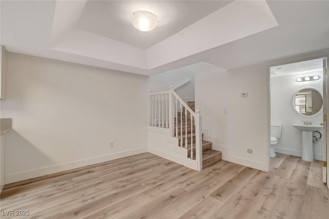 stairway with a tray ceiling, baseboards, and wood finished floors