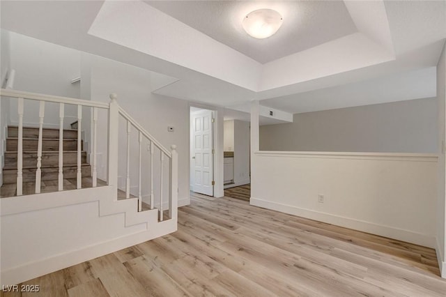 empty room with stairs, a raised ceiling, wood finished floors, and baseboards