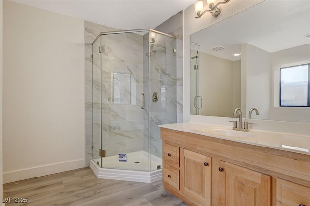 bathroom with vanity, wood finished floors, baseboards, and a marble finish shower