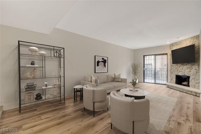 living area with a stone fireplace, baseboards, and wood finished floors