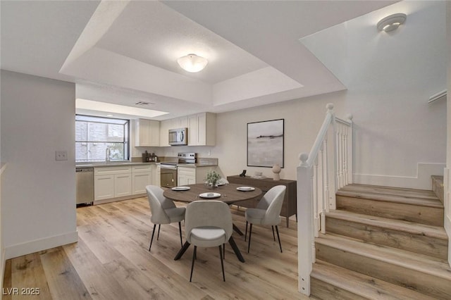 dining space with a raised ceiling, stairway, light wood-style floors, and baseboards