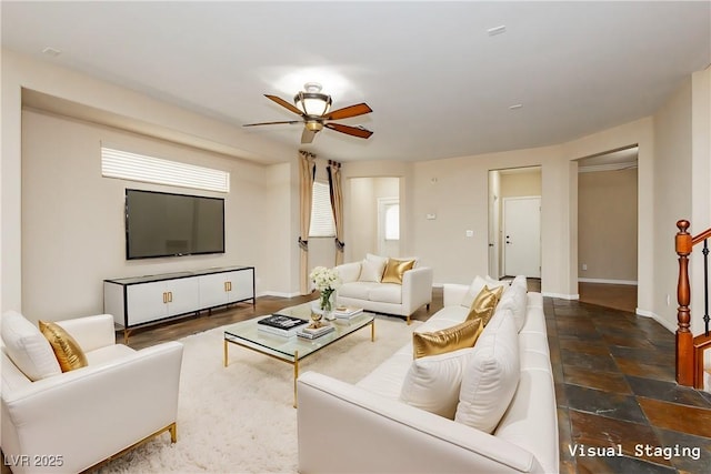 living area with baseboards, stone finish flooring, and ceiling fan