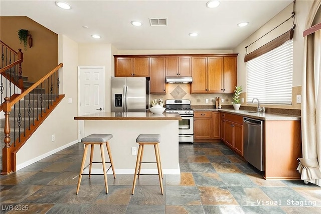 kitchen with visible vents, a kitchen island, a sink, stainless steel appliances, and under cabinet range hood