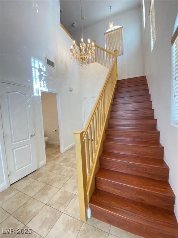 staircase featuring tile patterned flooring, a notable chandelier, a high ceiling, and visible vents