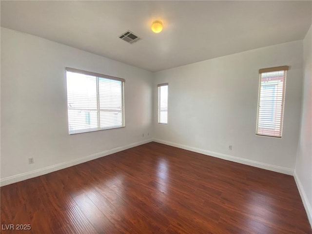 empty room featuring visible vents, baseboards, dark wood-type flooring, and a healthy amount of sunlight