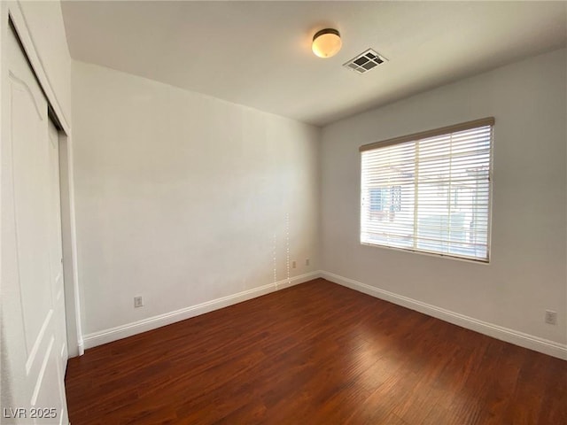 empty room with visible vents, dark wood-type flooring, and baseboards