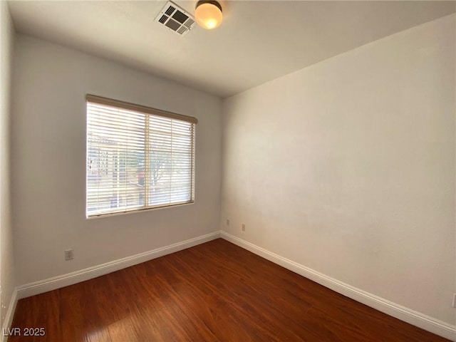 spare room with dark wood finished floors, visible vents, and baseboards