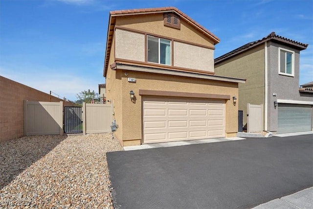 traditional-style house featuring aphalt driveway, stucco siding, an attached garage, and a gate