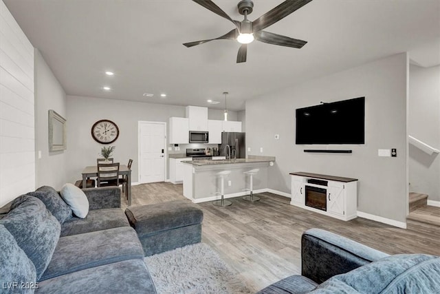 living room with stairway, baseboards, a ceiling fan, and wood finished floors