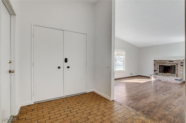 entrance foyer featuring baseboards, high vaulted ceiling, wood finished floors, and a fireplace